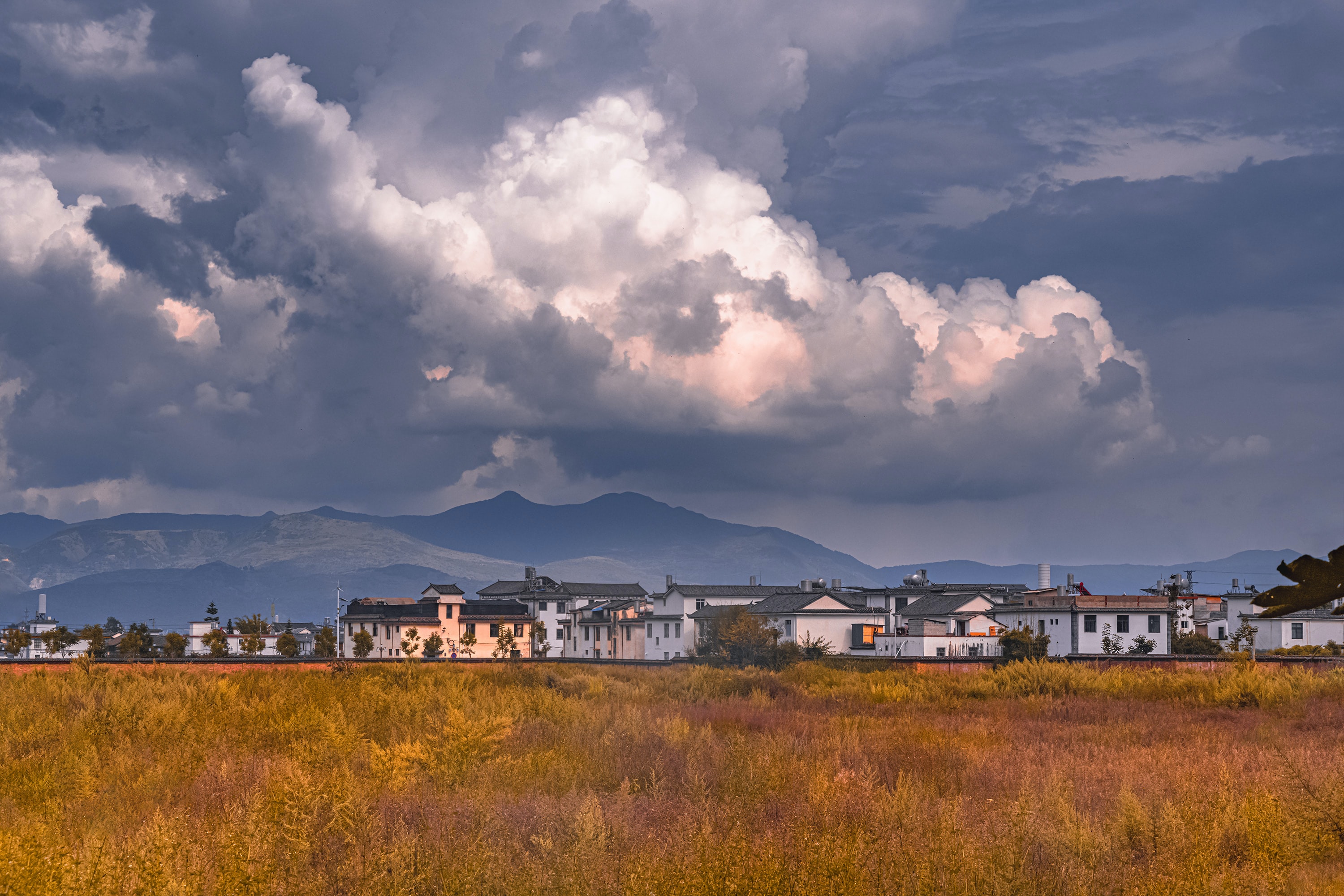 Wolkendecke über einer Landschaft mit Häusern © Yue Su | Unsplash